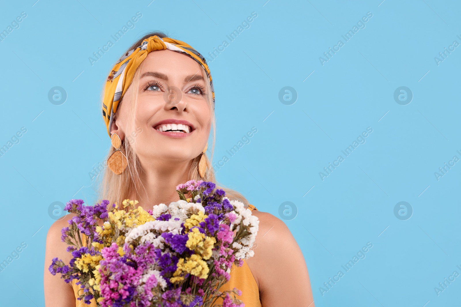 Photo of Portrait of smiling hippie woman with bouquet of flowers on light blue background. Space for text