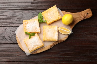 Photo of Tasty lemon bars powdered with sugar and mint on wooden table, top view