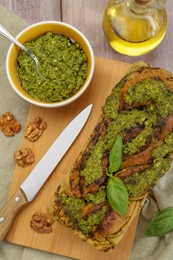 Freshly baked pesto bread with basil and knife on wooden table, flat lay
