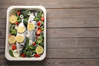 Photo of Raw fish with vegetables and lemon in baking dish on wooden table, top view. Space for text