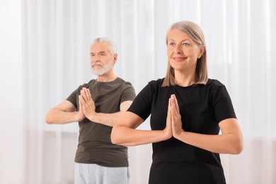 Senior couple practicing yoga indoors, selective focus