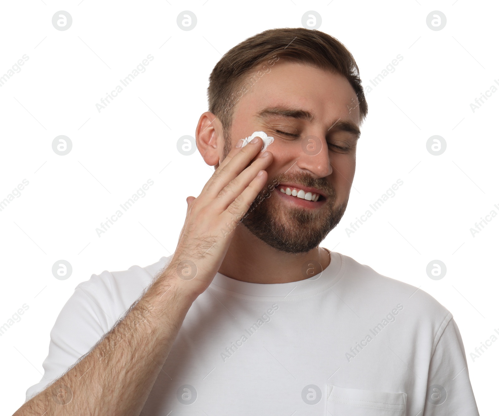 Photo of Happy young man applying facial cream on white background