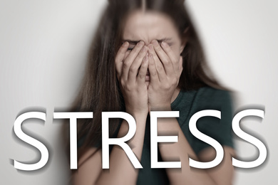 Image of Word STRESS and depressed young woman crying on light background 