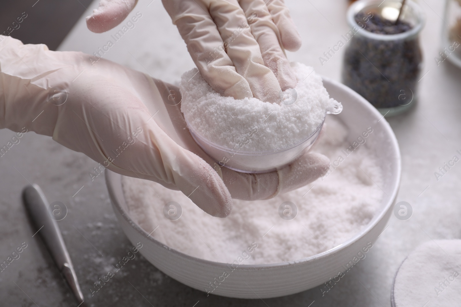 Photo of Woman in gloves making bath bomb at grey table, closeup