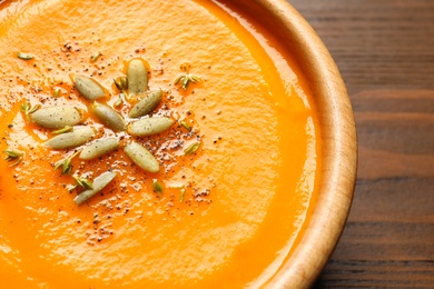 Tasty pumpkin soup with seeds in bowl on wooden table, closeup