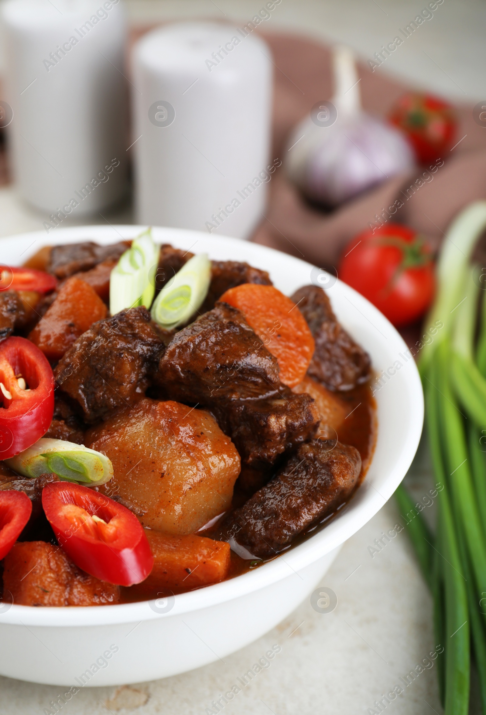 Photo of Delicious beef stew with carrots, chili peppers, green onions and potatoes on white textured table, closeup