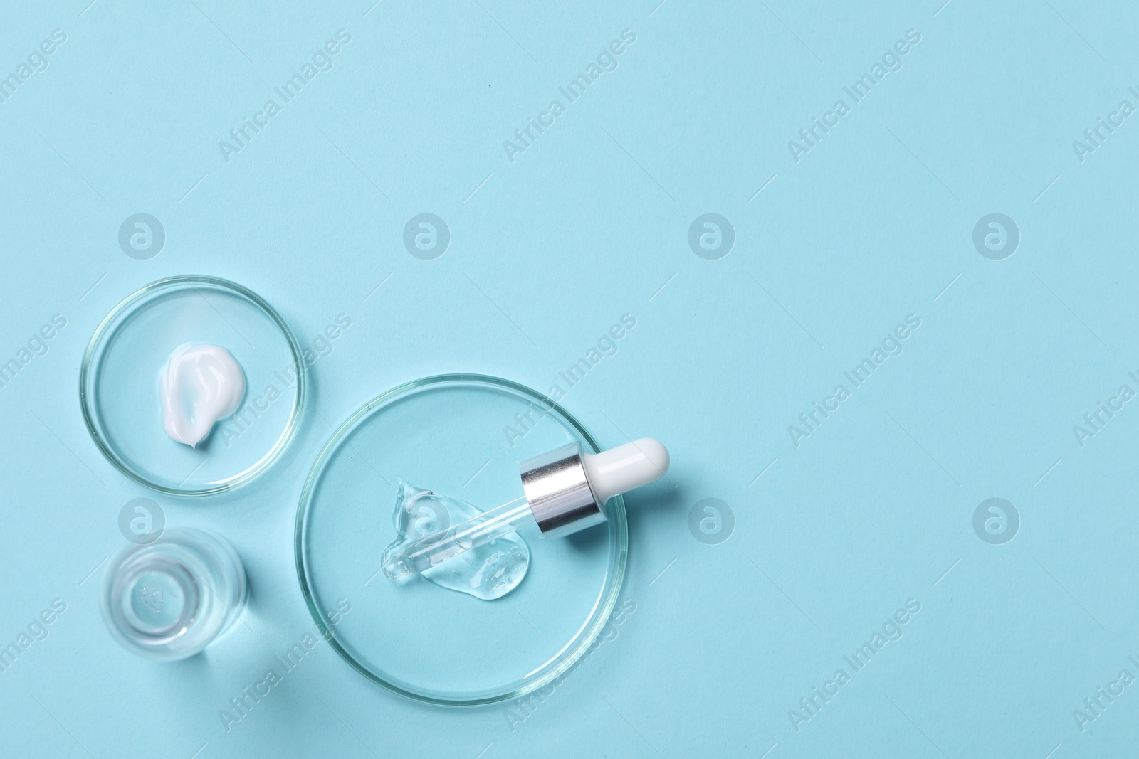 Photo of Petri dishes with samples of cosmetic serums, bottle and pipette on light blue background, flat lay. Space for text