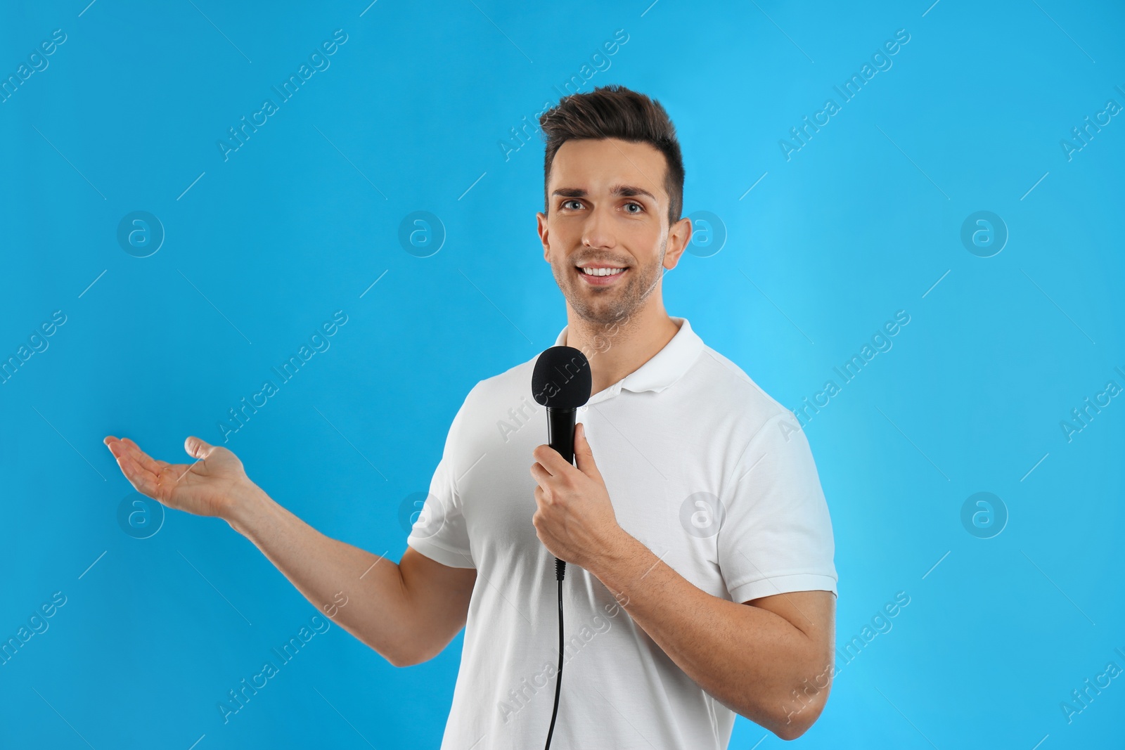 Photo of Young male journalist with microphone on blue background