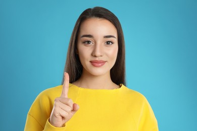 Photo of Woman showing number one with her hand on light blue background