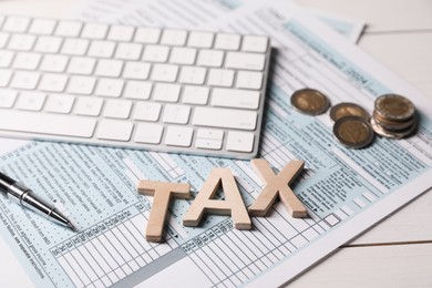 Photo of Word Tax made with letters, documents, keyboard, coins and pen on white wooden table, closeup