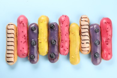 Photo of Delicious eclairs covered with glaze on light blue background, top view