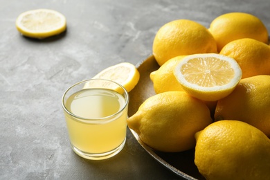 Photo of Plate with ripe lemons and glass of fresh juice on table