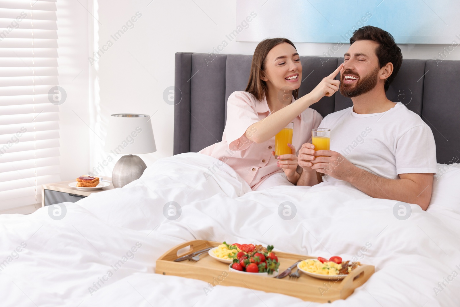 Photo of Happy couple eating tasty breakfast in bed at home. Space for text