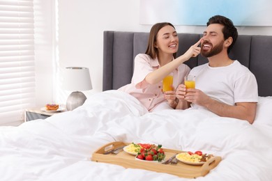 Photo of Happy couple eating tasty breakfast in bed at home. Space for text