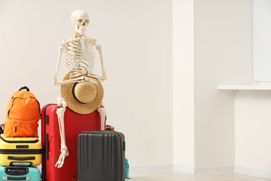 Photo of Waiting concept. Human skeleton with hat and suitcases indoors, space for text