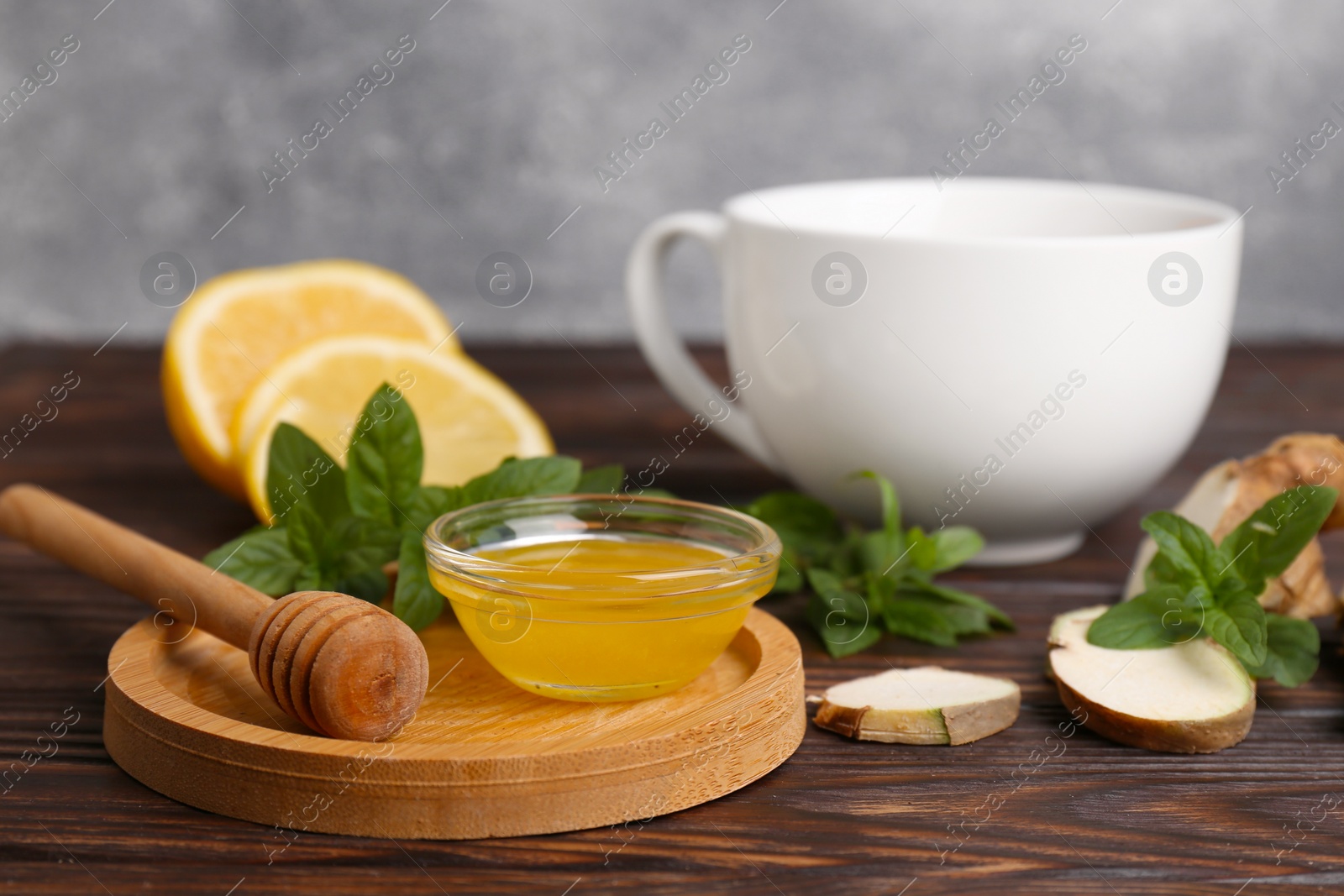 Photo of Bowl with honey for tea, lemon, mint and ginger on wooden table