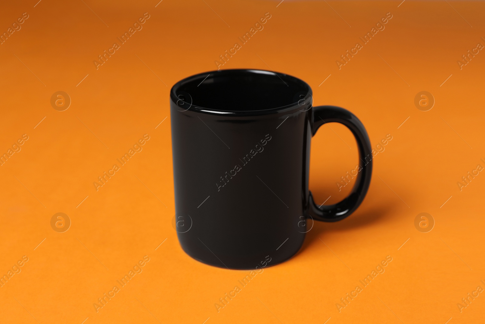 One black ceramic mug on orange background Photo of One black ceramic mug on orange background