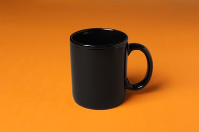 Photo of One black ceramic mug on orange background