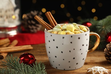 Photo of Delicious hot chocolate with marshmallows, cinnamon and Christmas decor on wooden table against blurred festive lights, closeup