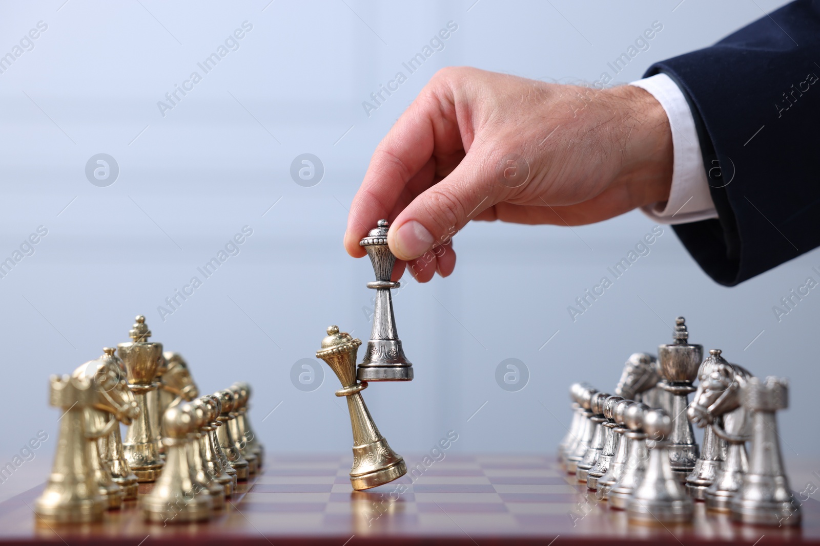 Photo of Man with bishop game piece playing chess at checkerboard against grey background, closeup