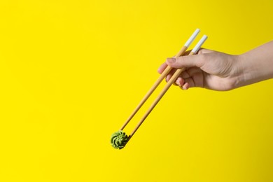 Photo of Woman holding swirl of wasabi paste with chopsticks on yellow background, closeup. Space for text