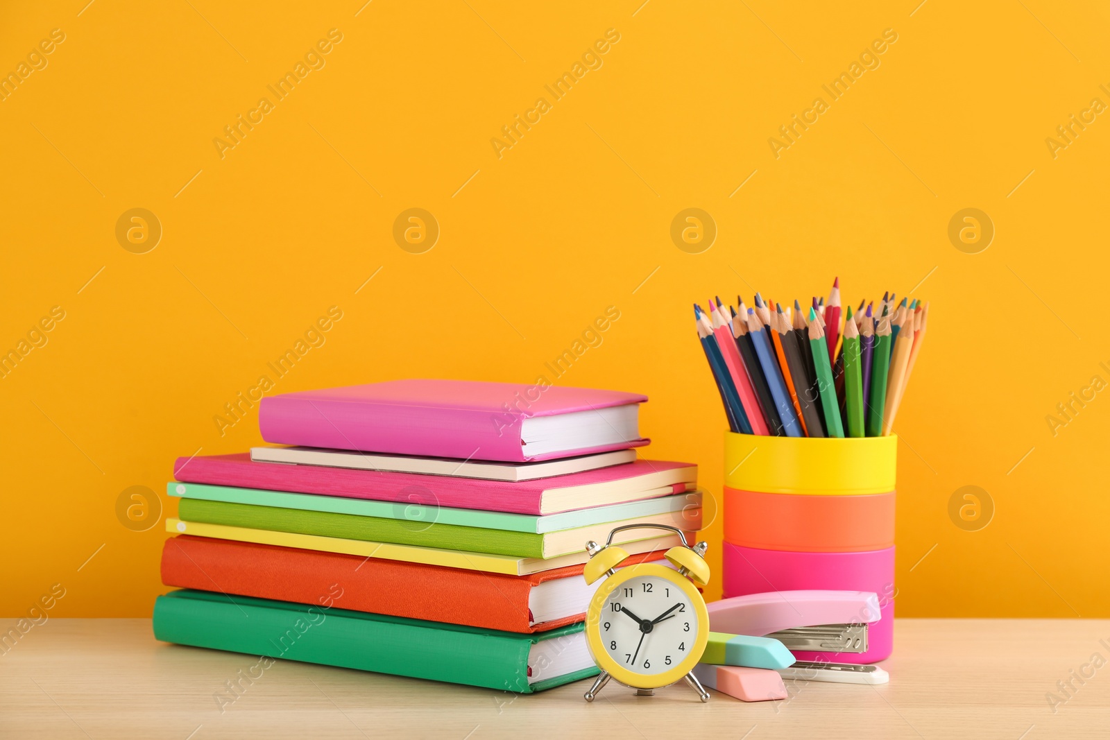 Photo of Different school stationery and alarm clock on table against orange background, space for text. Back to school