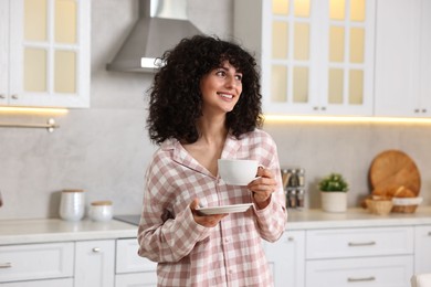 Photo of Beautiful young woman in stylish pyjama with cup of drink in kitchen