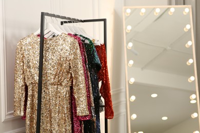 Clothing rack with colorful sequin party dresses on hangers near mirror in boutique, space for text