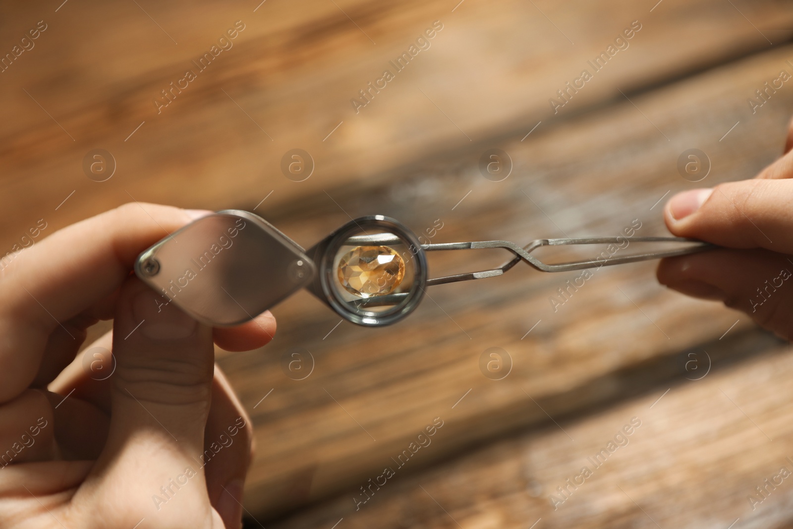 Photo of Male jeweler evaluating precious gemstone at table in workshop, closeup