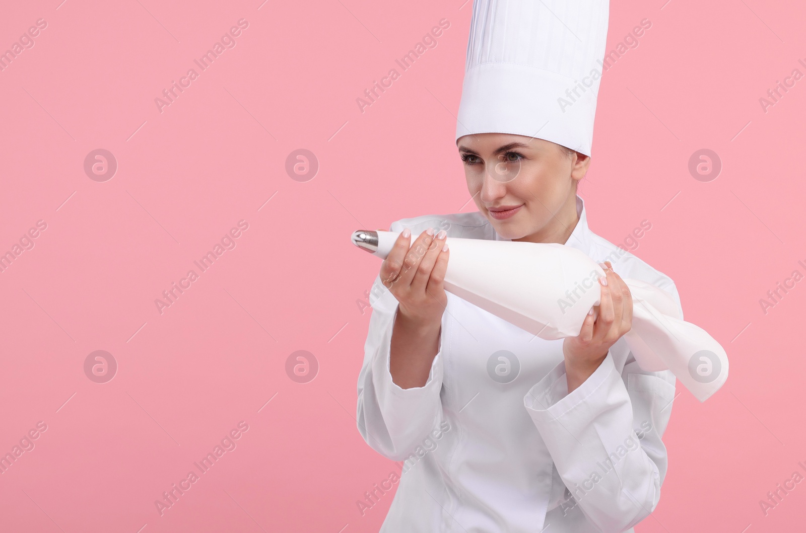 Photo of Professional confectioner in uniform holding piping bag on pink background. Space for text