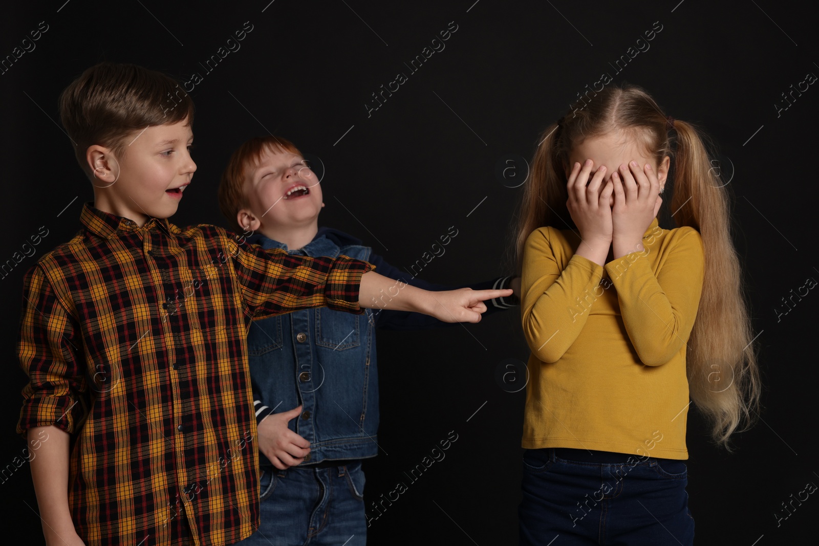 Photo of Boys laughing and pointing at upset girl on black background. Children's bullying