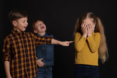 Photo of Boys laughing and pointing at upset girl on black background. Children's bullying
