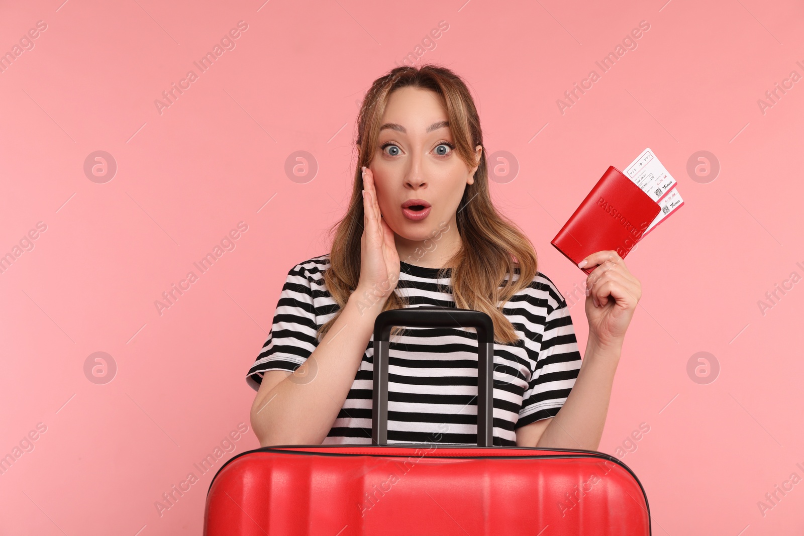 Photo of Emotional young woman with passport, ticket and suitcase on pink background