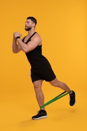 Photo of Young man exercising with elastic resistance band on orange background