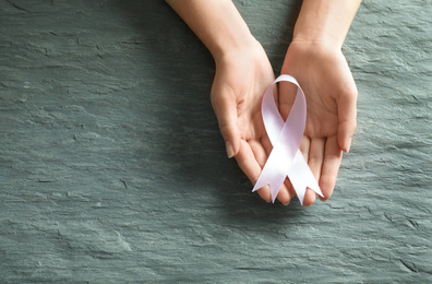 Woman holding pink ribbon on grey stone background, top view with space for text. Breast cancer awareness