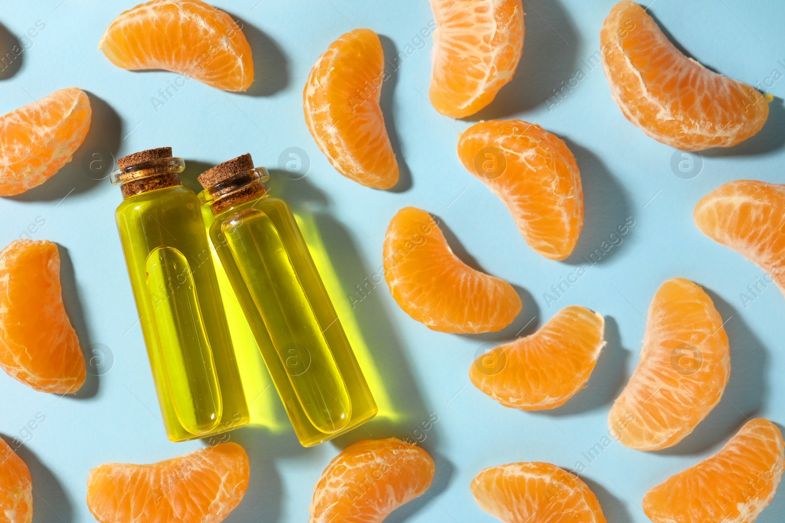 Photo of Aromatic tangerine essential oil in bottles and citrus fruits on light blue table, flat lay