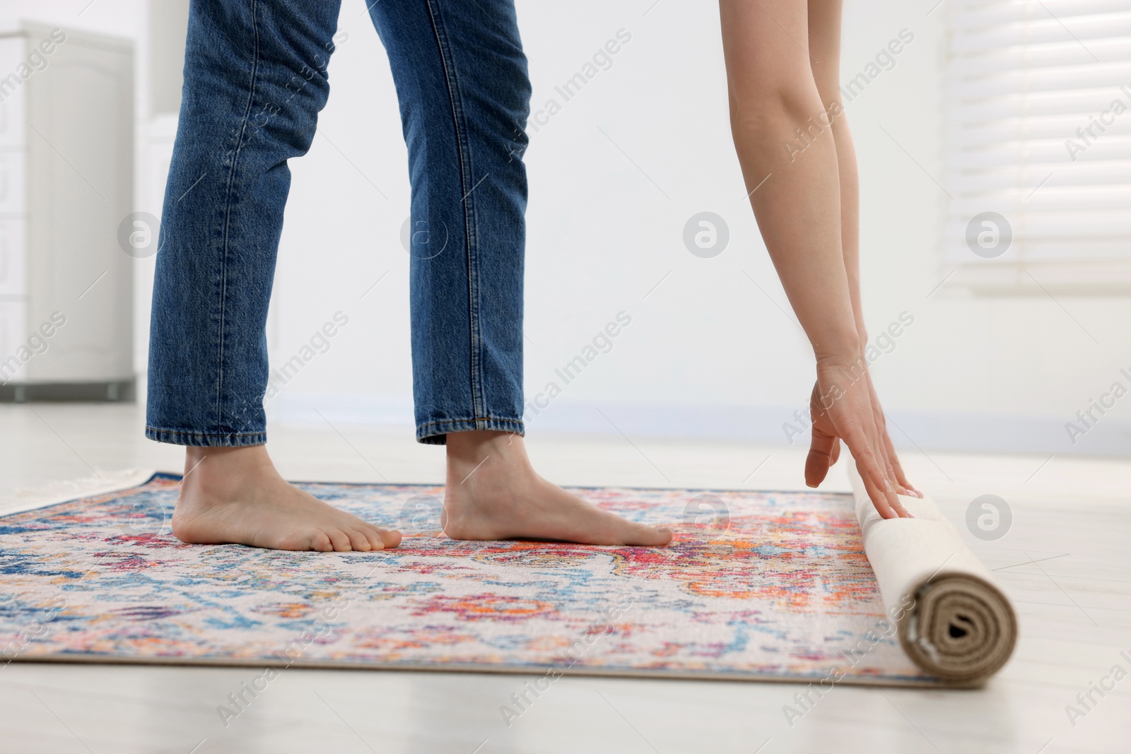 Photo of Woman unrolling carpet with beautiful pattern on floor in room, closeup