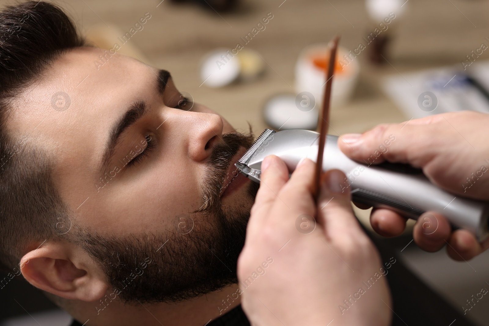 Photo of Professional barber trimming client's mustache in barbershop, closeup