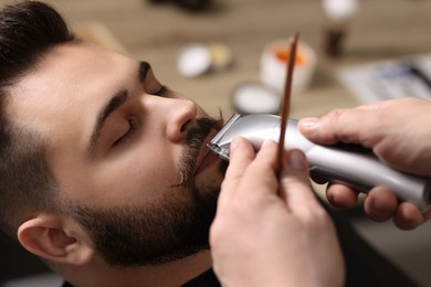 Photo of Professional barber trimming client's mustache in barbershop, closeup