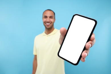 Young man showing smartphone in hand on light blue background, selective focus. Mockup for design