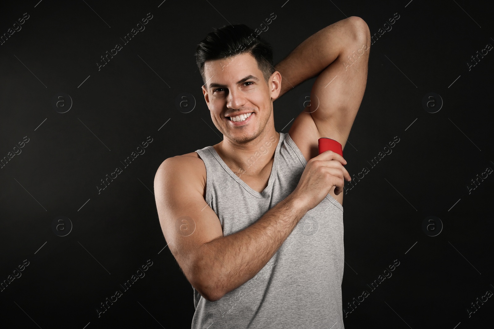 Photo of Handsome man applying deodorant to armpit on black background