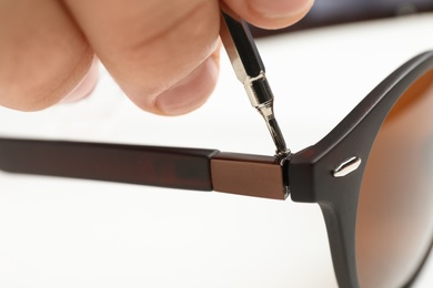 Photo of Handyman repairing sunglasses with screwdriver on white background, closeup