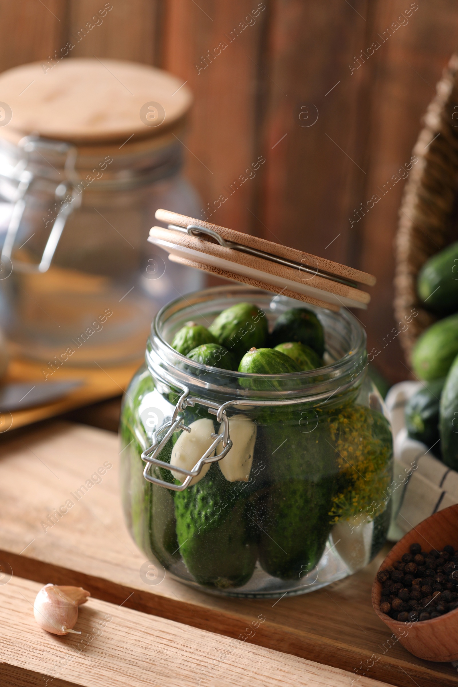 Photo of Glass jar with fresh cucumbers and other ingredients on wooden table. Canning vegetable