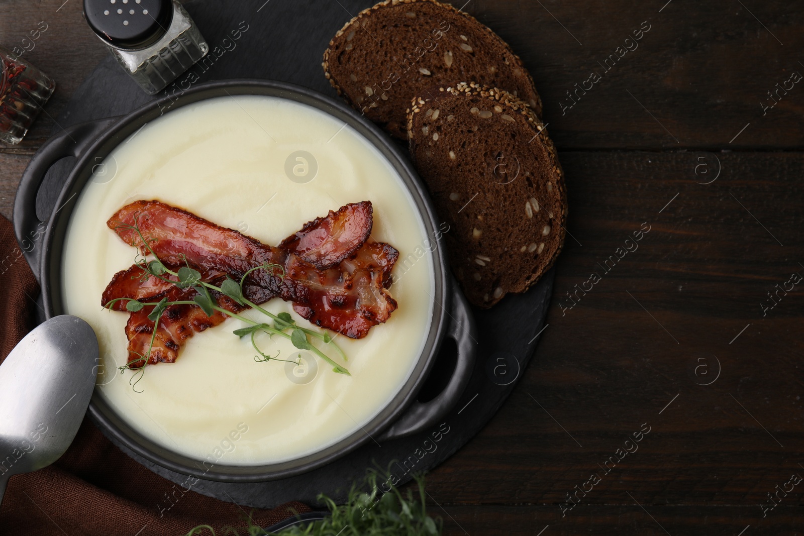 Photo of Delicious potato soup with bacon and microgreens in bowl served on wooden table, flat lay. Space for text