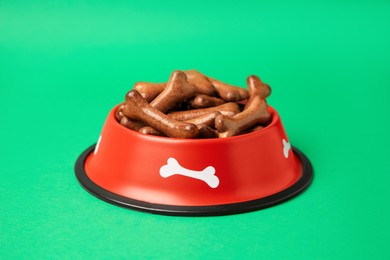 Photo of Red bowl with bone shaped dog cookies on green background