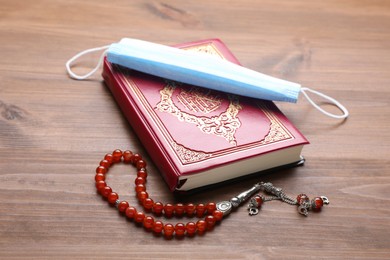 Photo of Muslim prayer beads, Quran and medical mask on wooden table