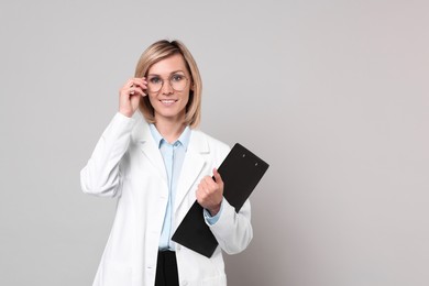 Photo of Smiling doctor with clipboard on grey background. Space for text