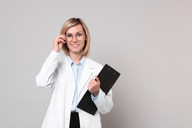 Smiling doctor with clipboard on grey background. Space for text