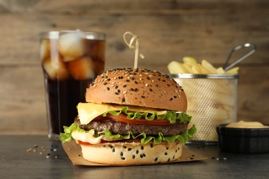 Photo of Burger with delicious patty, soda drink, french fries and sauce on gray table