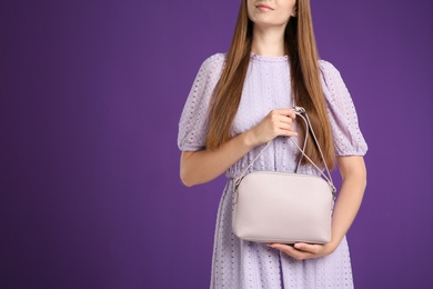 Young woman with stylish pink bag on purple background, closeup. Space for text